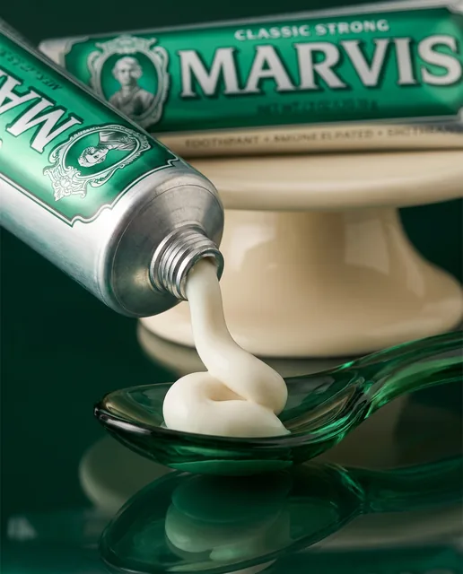 A close view of Marvis toothpaste curling into an emerald glass spoon