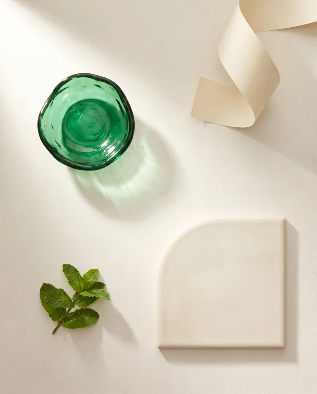 Newly generated material reference: emerald glass, curved ivory ceramic, a paper curl and fresh mint arranged on a light worktable