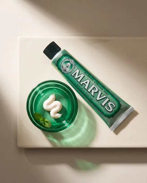 The Marvis tube and an emerald dish of toothpaste arranged on a pale ceramic slab