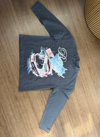 Original phone photo of the charcoal Christian Rose graphic top laid out on a wooden floor