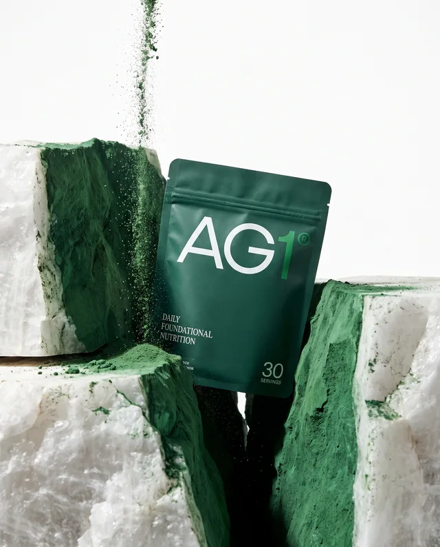 A green AG1 pouch emerging from a split white and green stone block