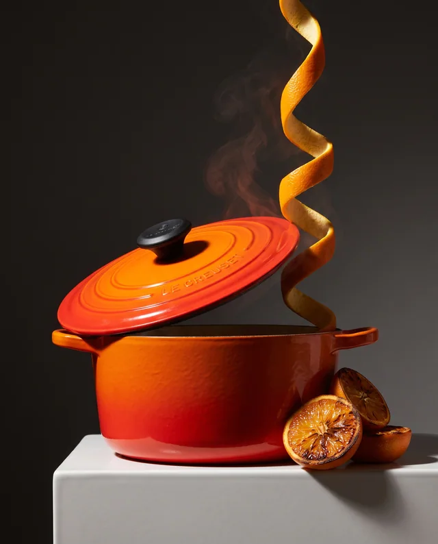 An orange Le Creuset casserole with a lifted lid and curling steam