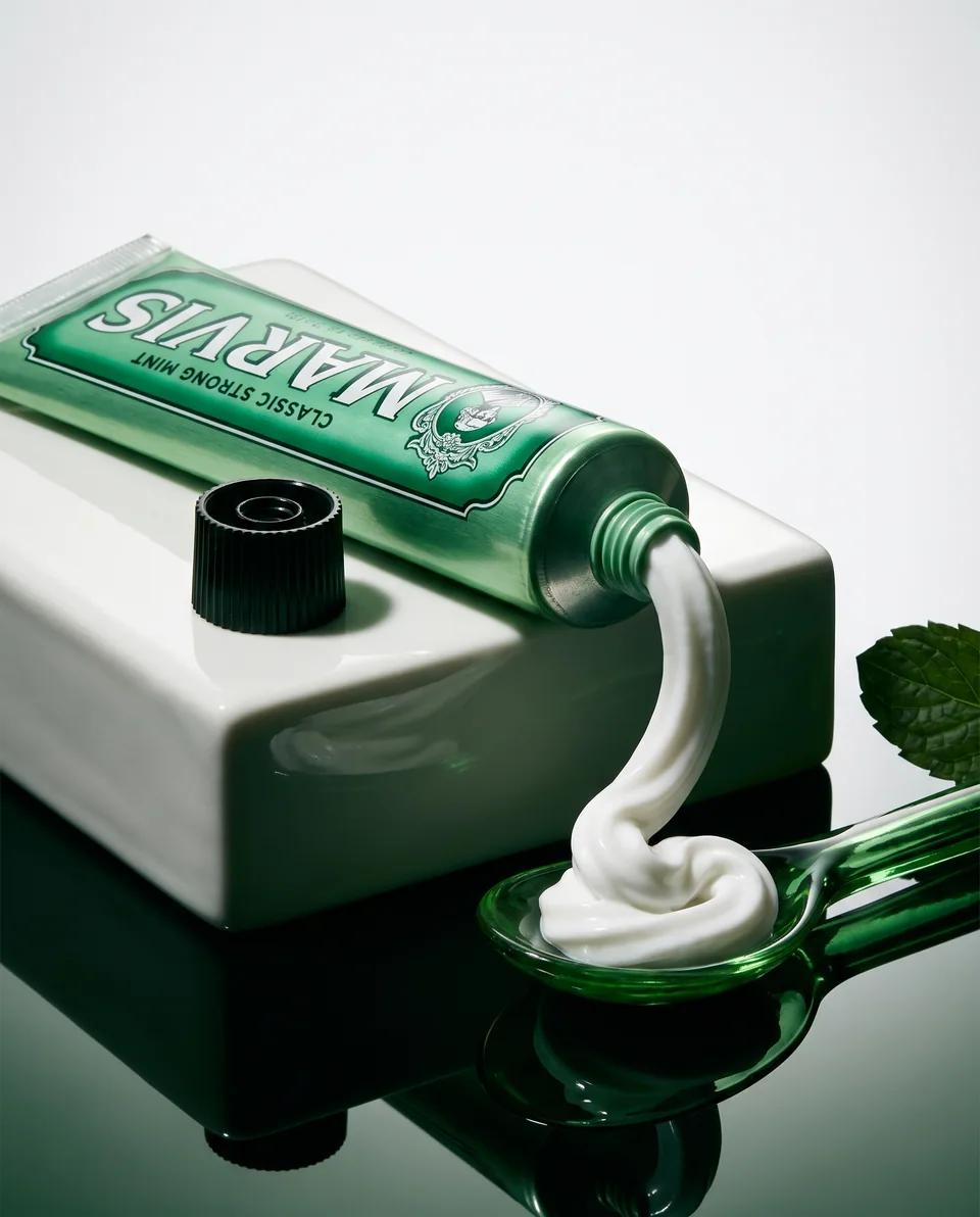 Marvis toothpaste curling into an emerald glass spoon beside a white ceramic block in the Mint Ribbon studio concept