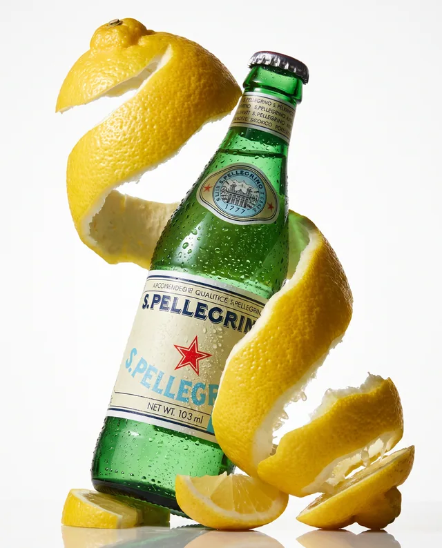 A green S.Pellegrino bottle wrapped in a suspended spiral of lemon peel